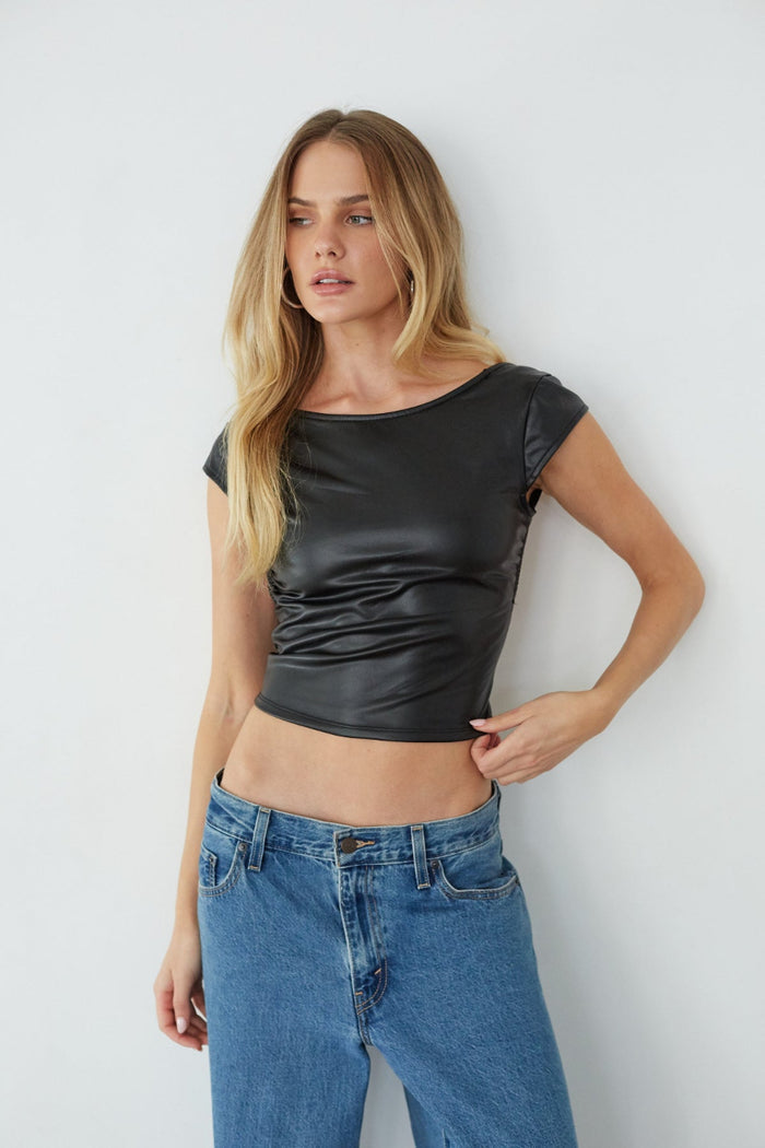 Woman wearing a black leather top and blue jeans against a white background