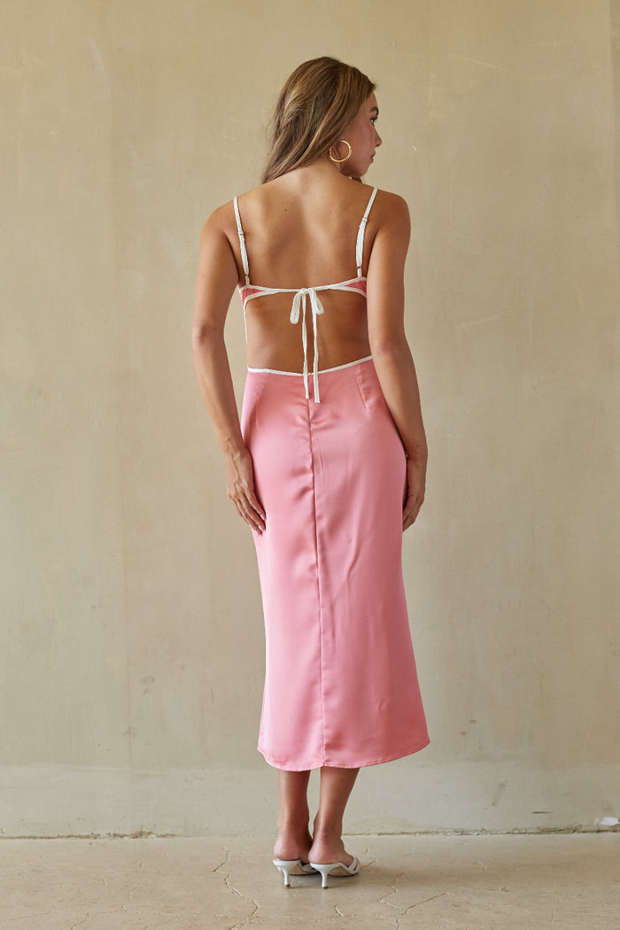 Woman wearing a pink skirt and white top against a beige wall.
