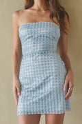 Woman wearing a strapless blue dress against a beige wall