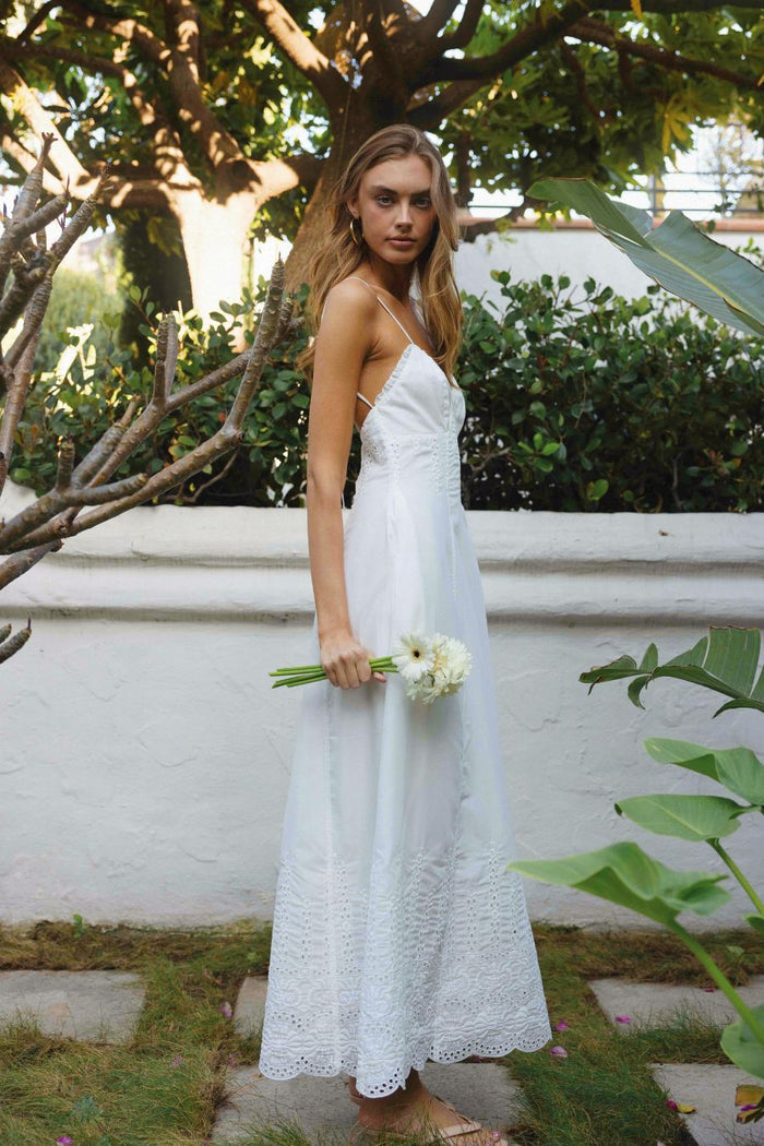 Woman in a white dress holding flowers in an outdoor setting