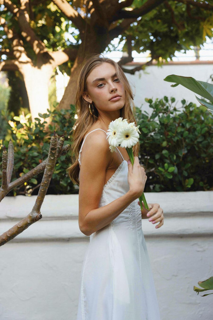 Woman in a white dress holding flowers in an outdoor setting