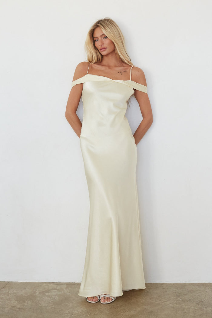 Woman wearing a long off-shoulder yellow dress against a white background
