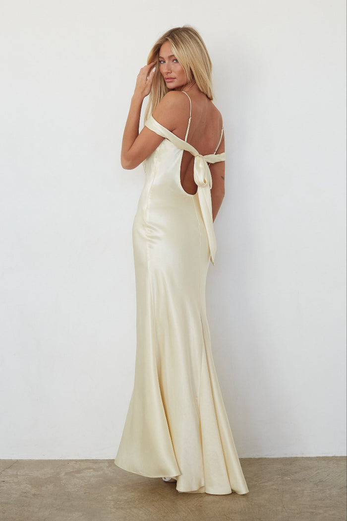 Woman wearing a yellow evening gown with cut-out back design against a plain background