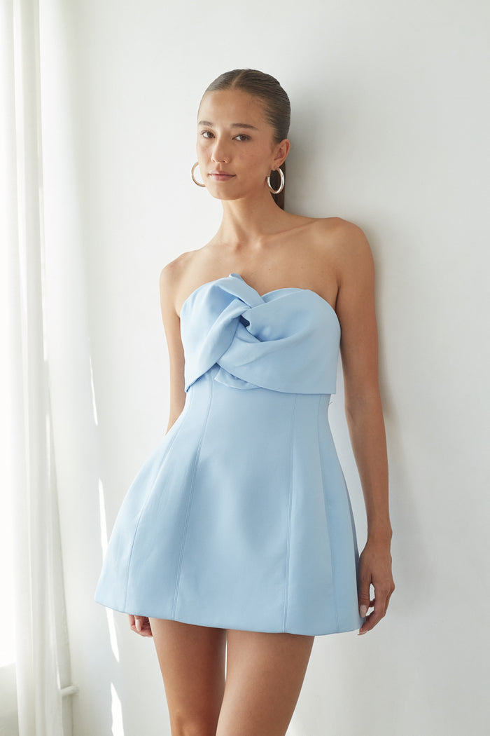 blue-image | front | Woman wearing a light blue strapless dress with a bow detail against a white background
