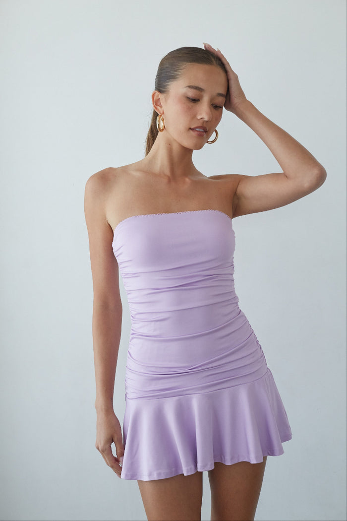 Woman wearing a light purple strapless dress against a plain background