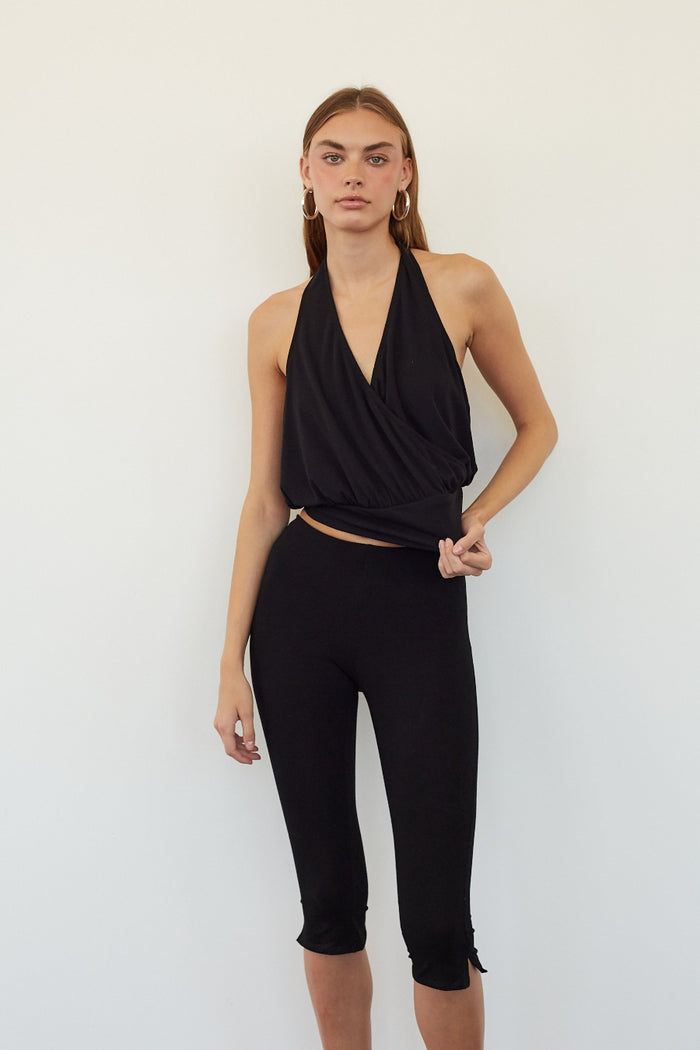 A woman modeling a black sleeveless halter-style wrap top and matching black capri leggings against a plain white studio background.