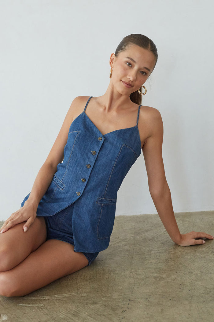 Woman wearing a blue denim outfit sitting on a concrete floor.