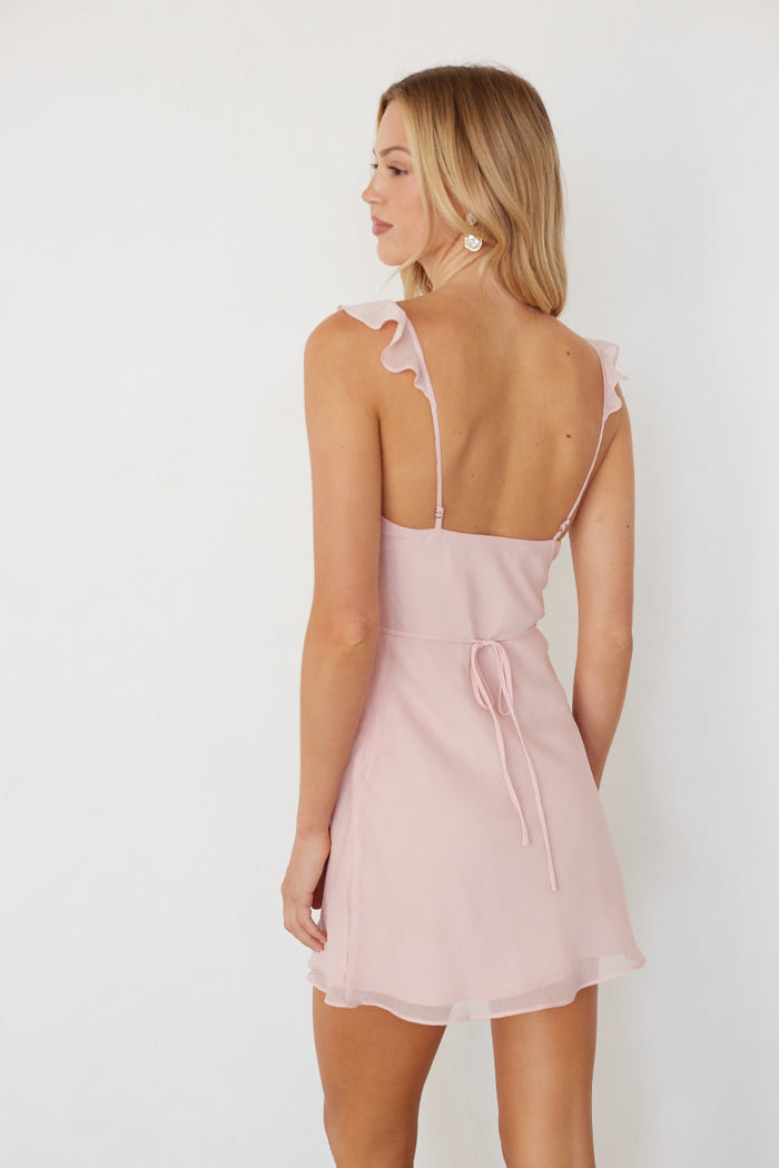 Woman wearing a light pink dress with thin straps against a white background
