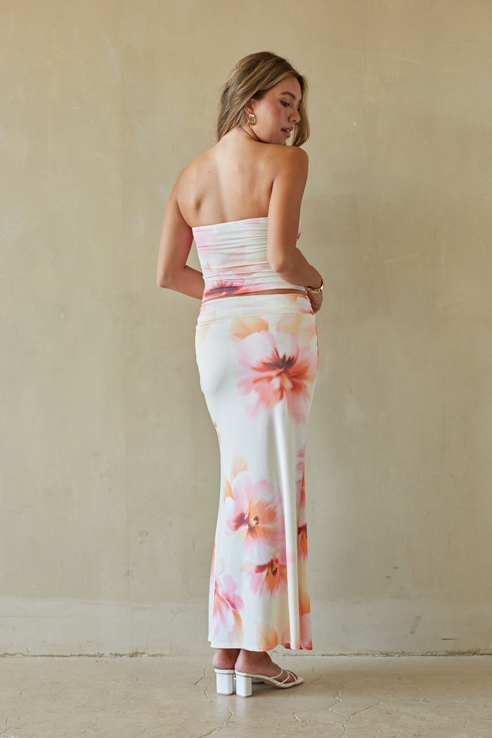 Woman wearing a floral strapless top and skirt set against a plain background