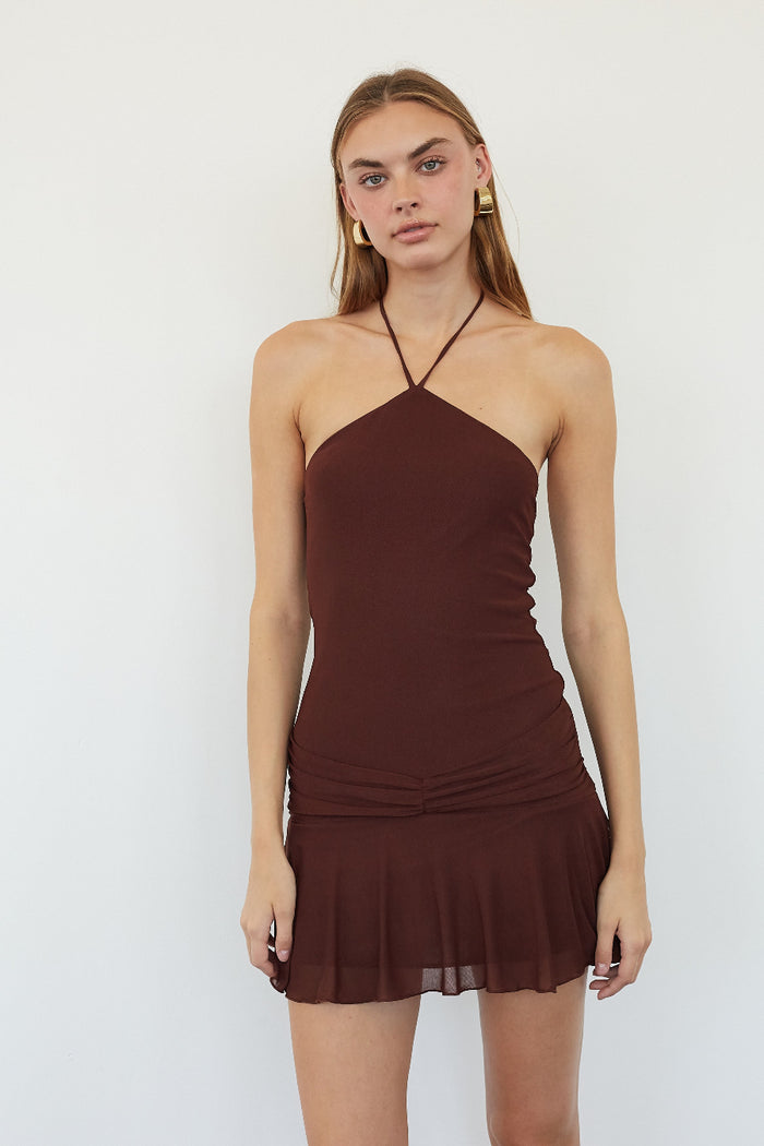 A woman modeling a dark brown halter-neck mini dress with a ruched waist and ruffled hem against a plain white studio background.