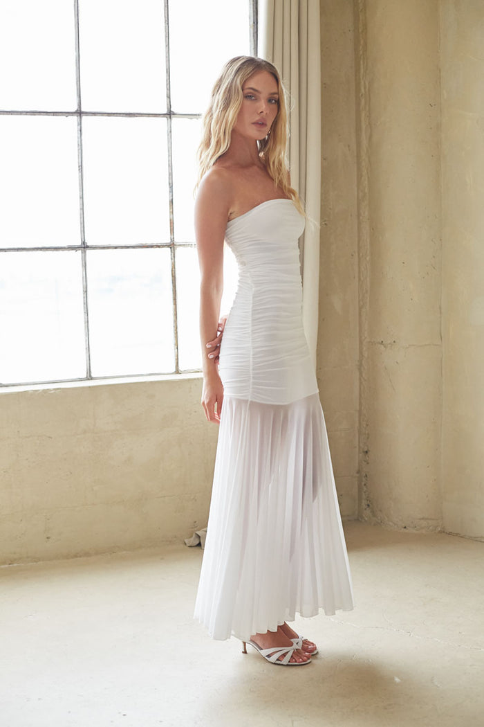 Woman wearing a white strapless dress standing in a room with large windows.