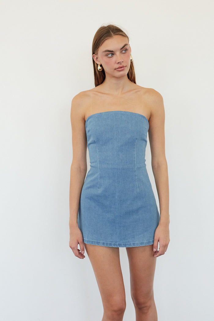 A woman modeling a strapless light blue denim mini dress against a plain white studio background.