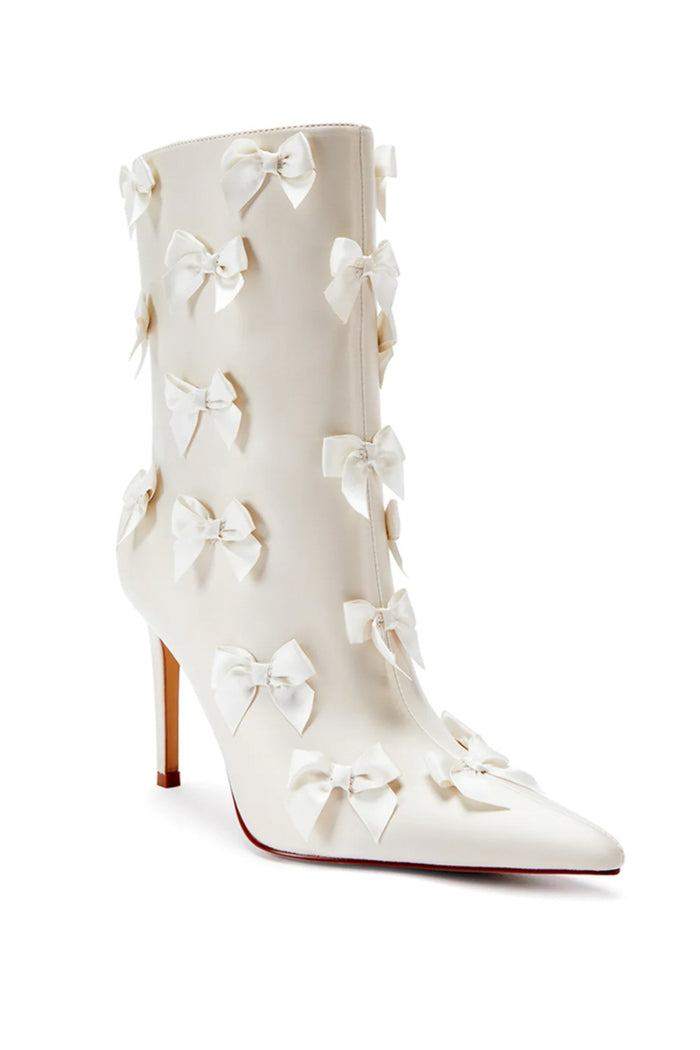 3/4 front/side view of a cream pointed toe satin stiletto  bootie with coquette style bows all over - perfect shoe for brides, birthday girls, and more