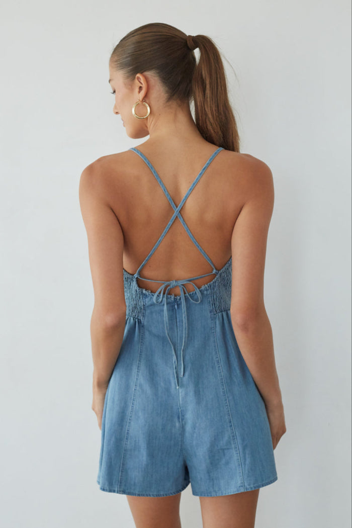 Woman wearing a blue denim romper with criss-cross straps on a plain background