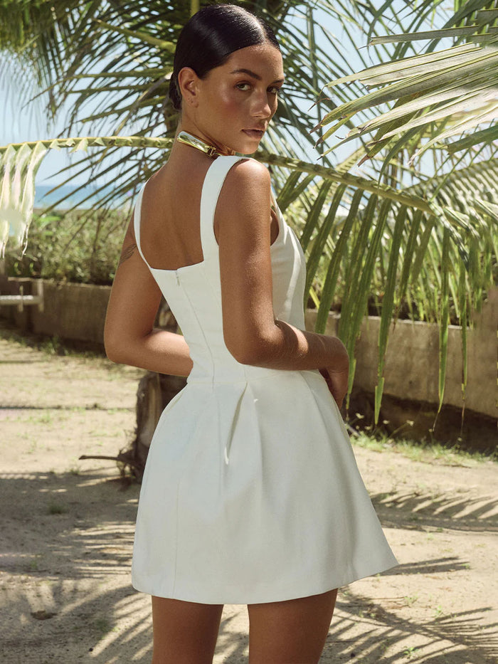 Woman in a white dress standing outdoors with palm trees in the background