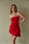 red-image | A woman in a strapless, royal blue mini dress with an asymmetrical hem and a high leg slit. The dress features an asymmetrical cinch detail with a side tie.
