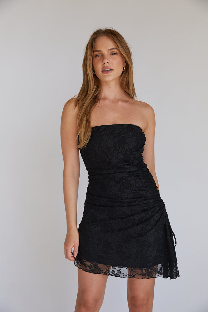 black-image | A woman in a strapless, royal blue mini dress with an asymmetrical hem and a high leg slit. The dress features an asymmetrical cinch detail with a side tie.