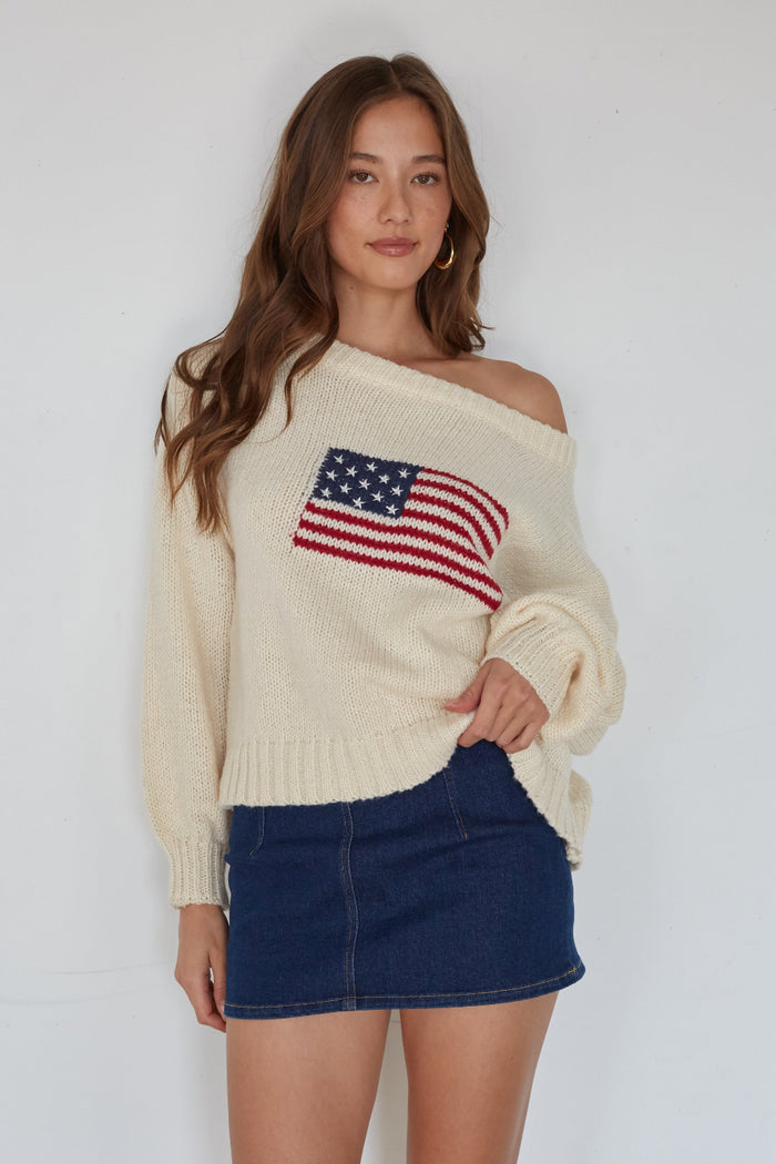 Woman wearing a cream sweater with an American flag design on a white background