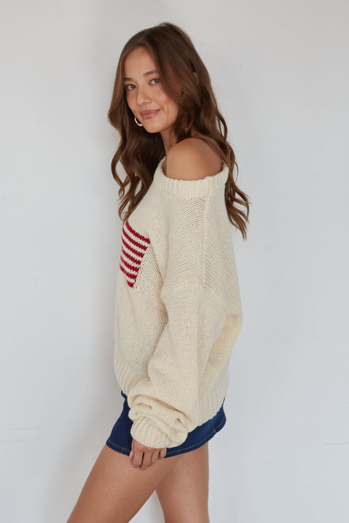 Woman wearing a cream sweater with a red and white pattern on a plain background