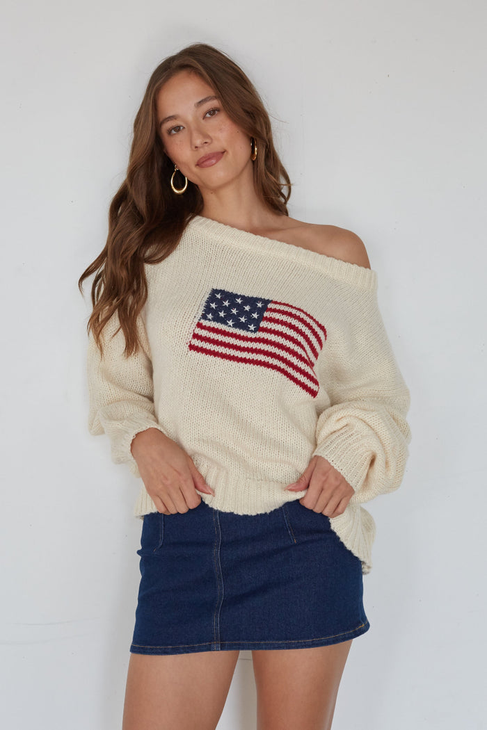 Woman wearing a cream sweater with an American flag design against a white background