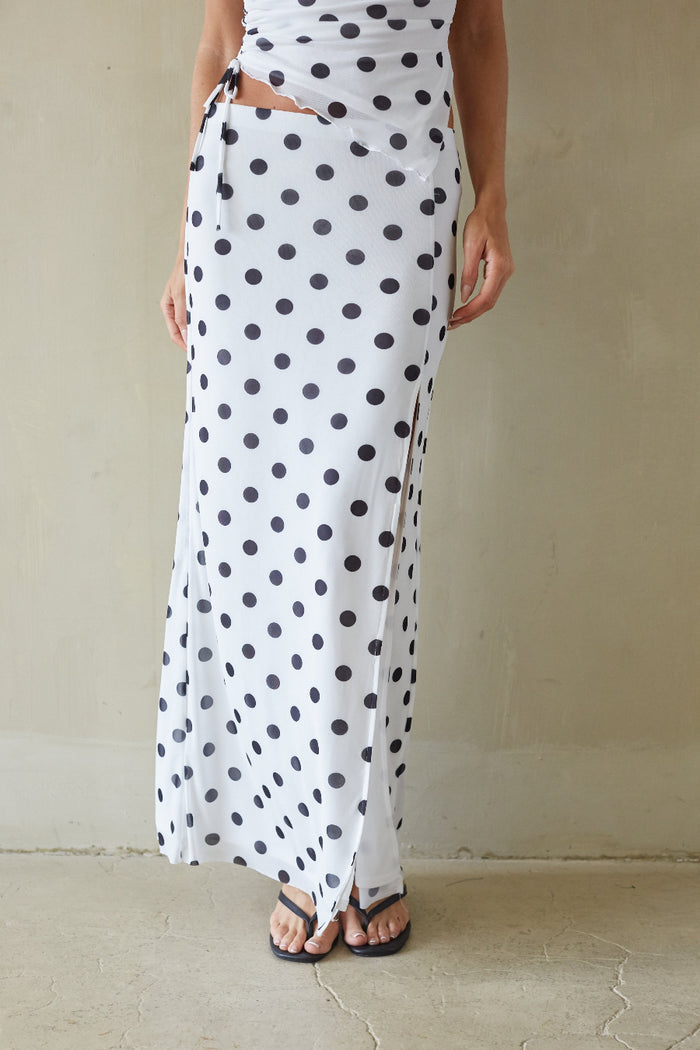 Person wearing a white dress with black polka dots against a plain background