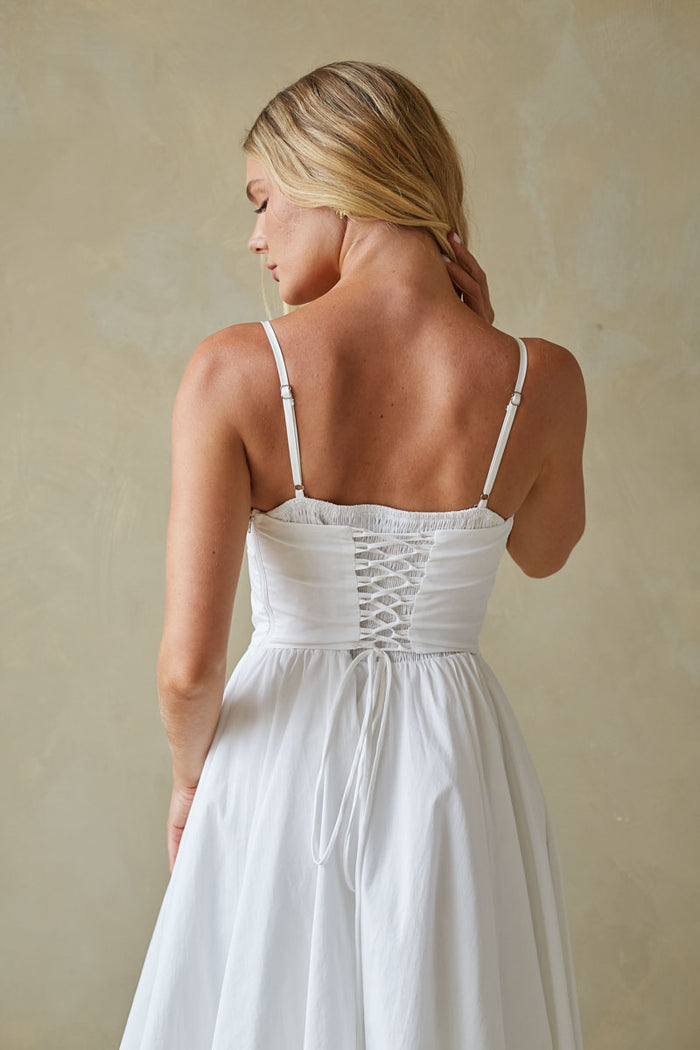 Woman wearing a white dress with thin straps and a lace-up back against a beige background