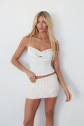 Woman wearing a white top and skirt against a plain background