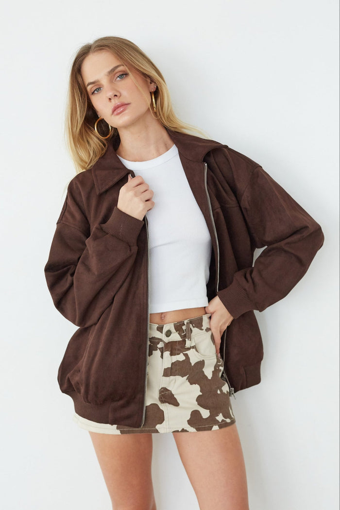 Woman wearing a brown jacket, white top, and patterned skirt against a white background