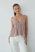 Woman wearing a striped halter top and white pants against a plain background