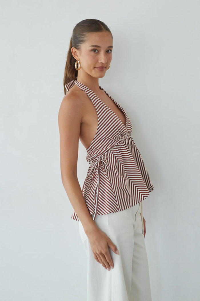 Woman wearing a striped halter top and white pants against a plain background