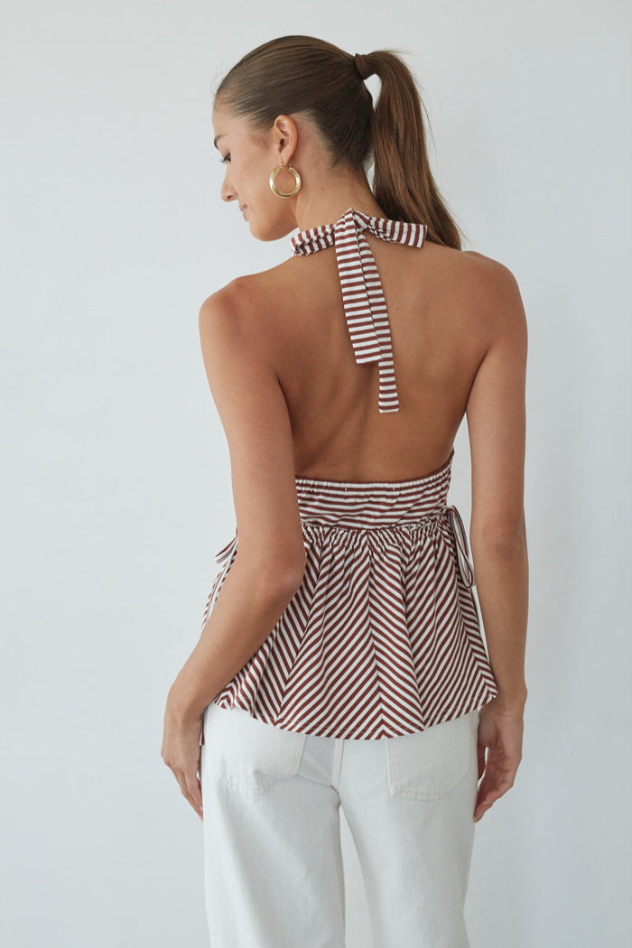 Woman wearing a striped halter top and white pants against a plain background