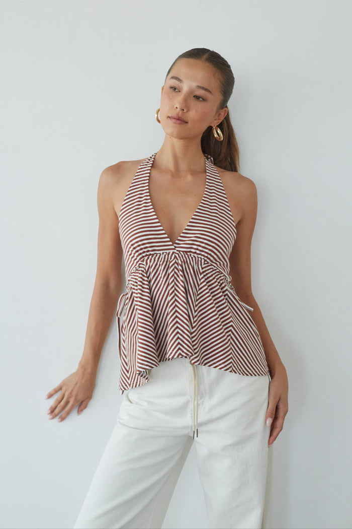 Woman wearing a striped halter top and white pants against a plain background