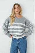 Woman wearing a gray and white striped sweater with blue jeans against a white background