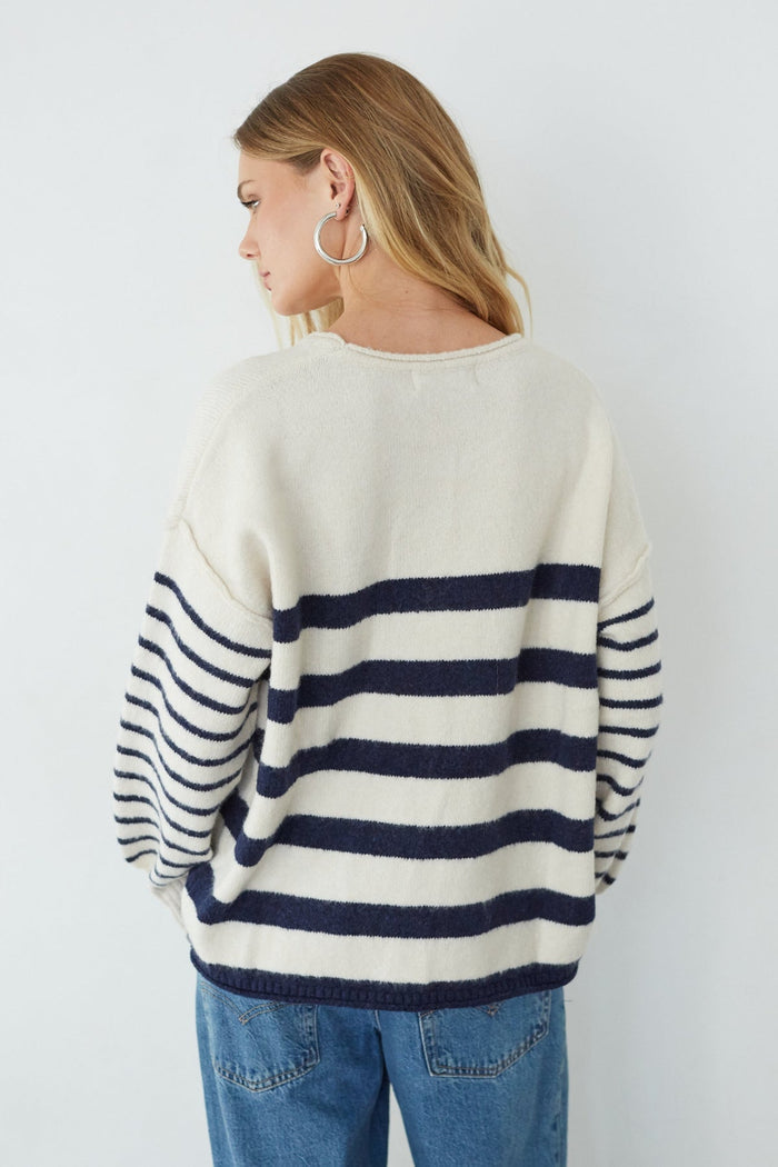 Person wearing a white and navy striped sweater with blue jeans on a plain background