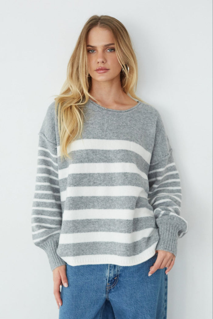 Woman wearing a gray and white striped sweater with blue jeans on a white background