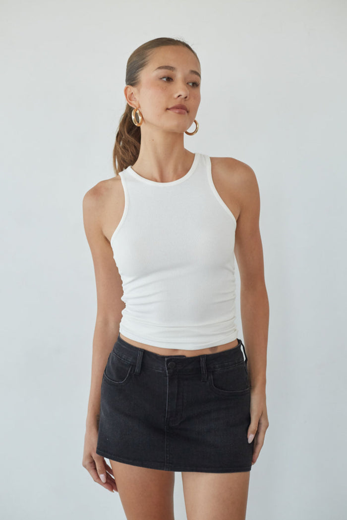 Woman wearing a white tank top and black skirt against a plain background