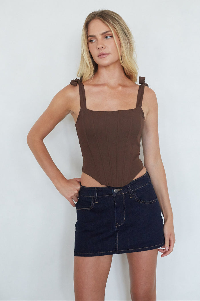 Woman wearing a brown tank top and dark denim skirt against a white background