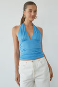 Woman wearing a blue halter top and white pants against a plain background