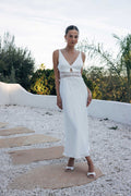 Woman in a white dress standing on a stone path with greenery in the background
