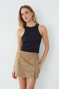 Woman wearing a black sleeveless top and beige suede skirt on a white background