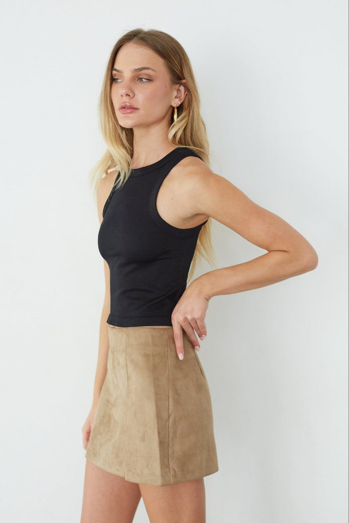 Woman wearing a black sleeveless top and beige skirt against a white background