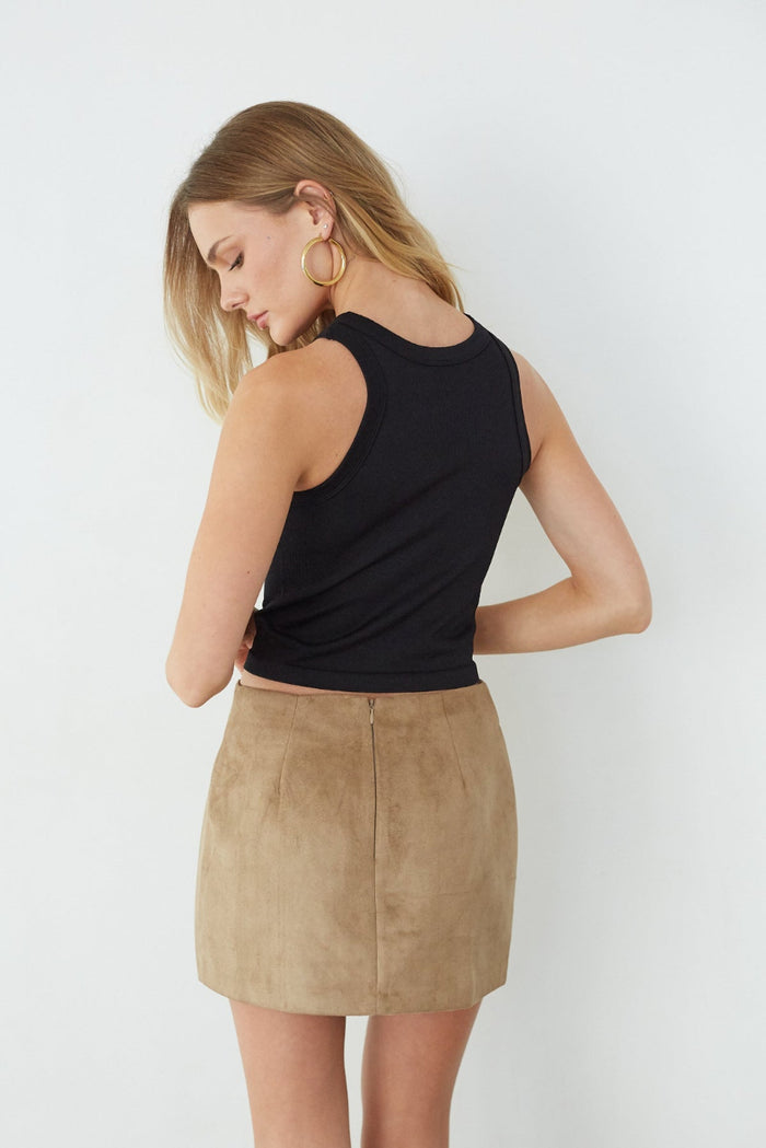 Woman wearing a black sleeveless top and beige suede skirt on a white background