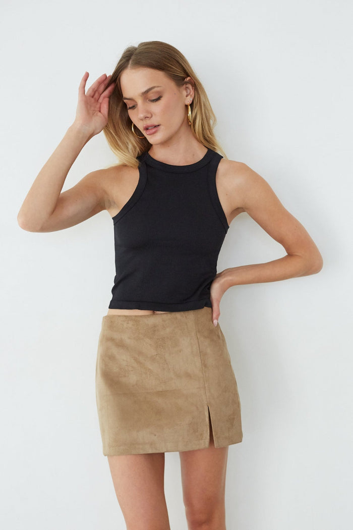 Woman wearing a black sleeveless top and beige suede skirt against a white background