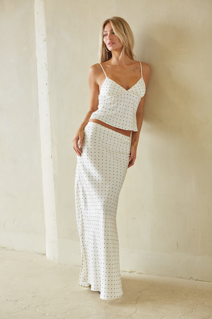 Woman wearing a white polka dot dress against a plain wall.