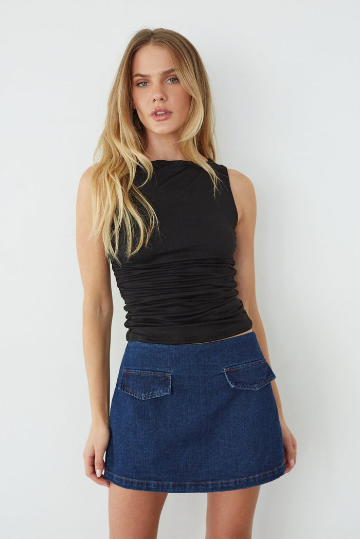 Woman wearing a black sleeveless top and blue denim skirt against a white background
