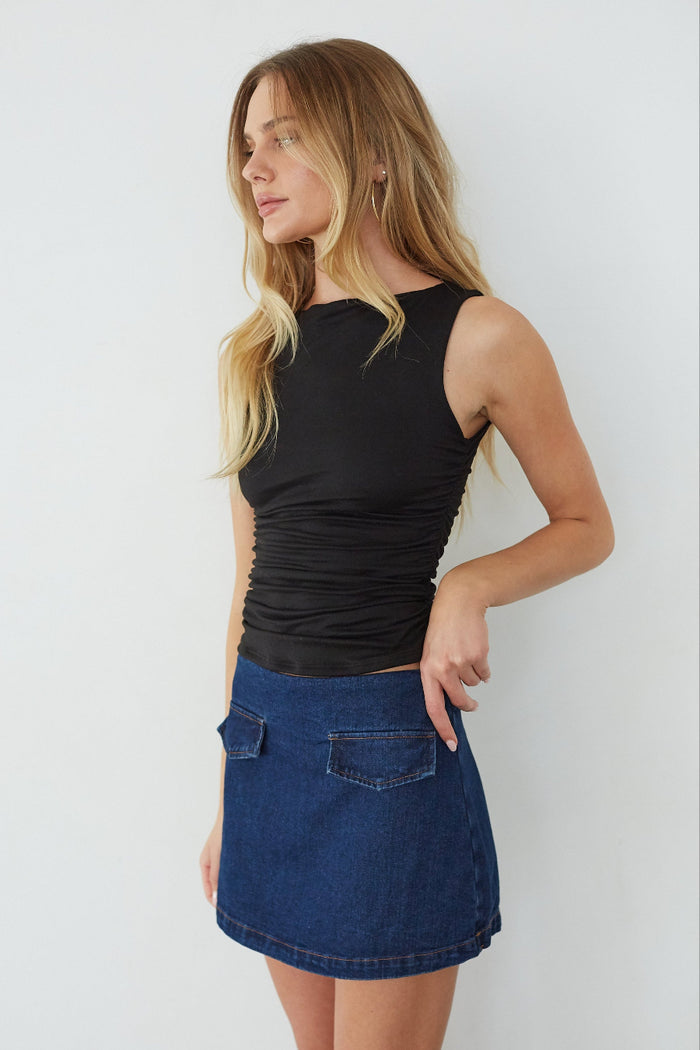 Woman wearing a black tank top and blue denim skirt against a white background