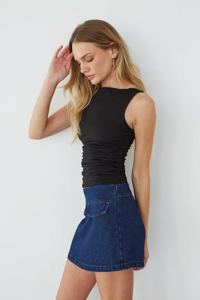Woman wearing a black sleeveless top and blue denim skirt against a white background