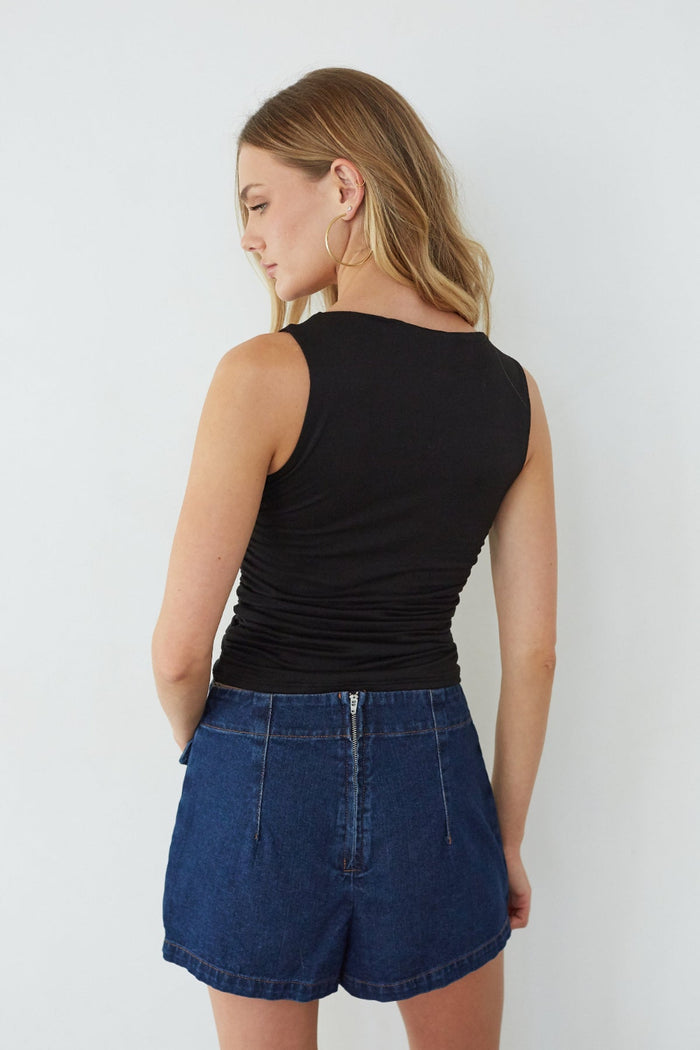 Woman wearing a black sleeveless top and blue denim shorts against a white background