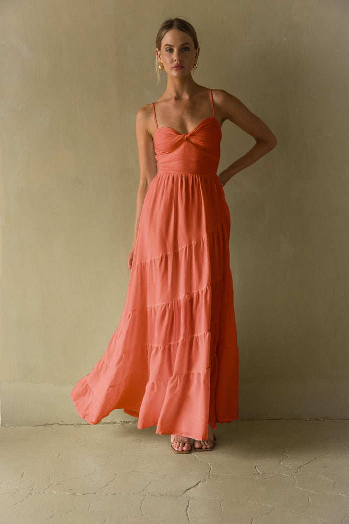 pink-image | A woman standing in a casual pose wearing a beige maxi dress with a twist front detail and tiered skirt.