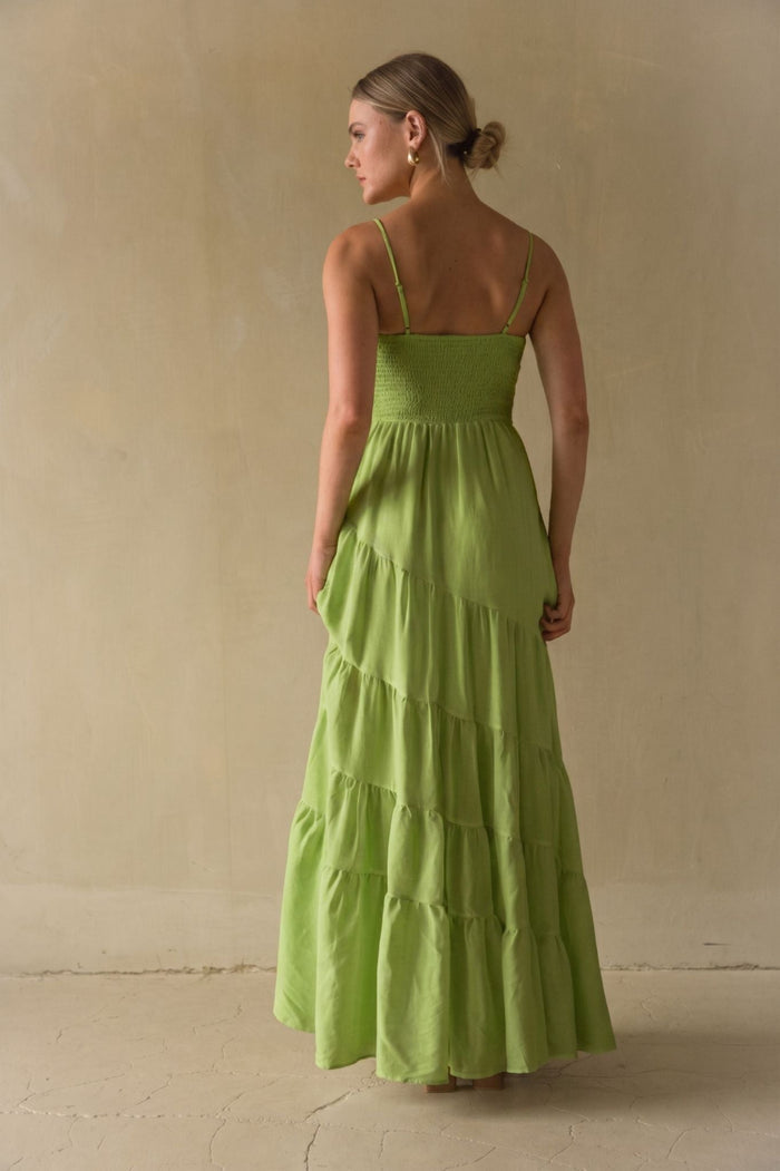 A woman wearing a bright lime green tiered maxi dress, shown from the back against a neutral beige plaster wall.